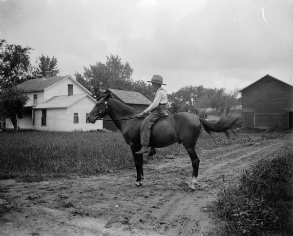 A young boy rides a horse without a saddle in a farm yard.