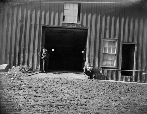 Two men relax against a barn doorway.