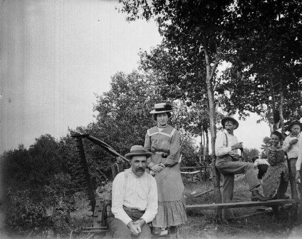 Several men and two women relax amidst farm machinery.