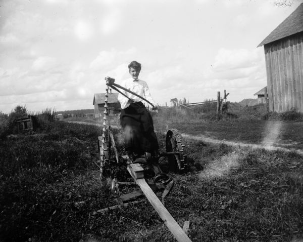 A woman sits on a piece of farm machinery, probably a mowing machine.