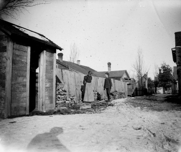 A woman and a boy stand near numerous piles of firewood and look at the leftover wood chippings.