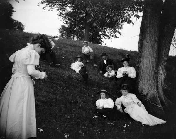 A woman takes a picture of a group of individuals relaxing on a hillside.