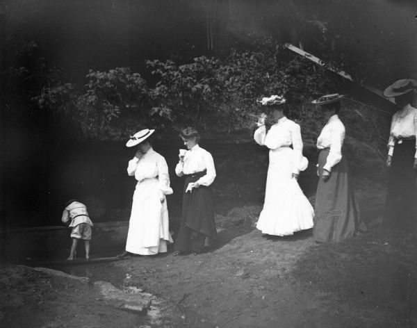 Five women and a child walk across a plank bridge to the spring at Rock Spring Park. The woman third from the left is Laura Jones.