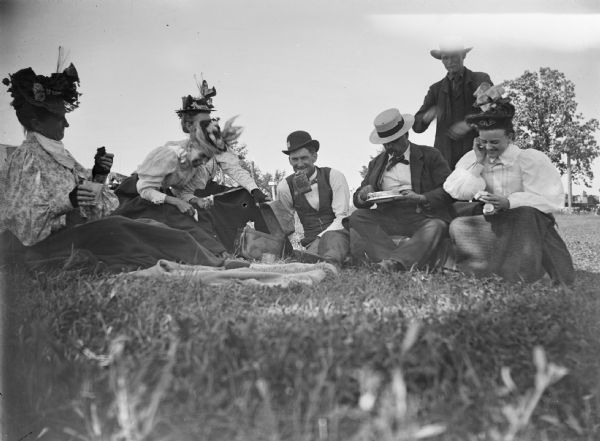 Three men and four women laugh while gathered for a picnic. From left to right Mrs. Charles J. Van Schaick and Grace Ogden are identified.	
