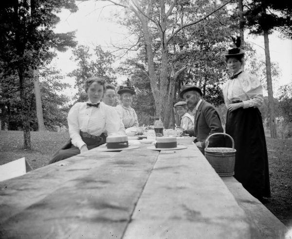 A man, boy, and three women sit around a picnic table. Another woman, probably Mrs. Charles Van Schaick, stands nearby.