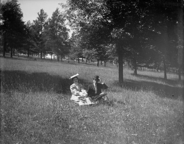 A man and woman sit in a wooded field.