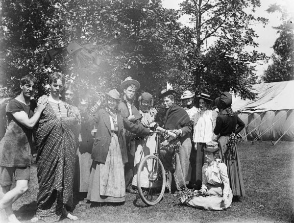 A large group of young men and women gather with a bicycle outside of a large tent.