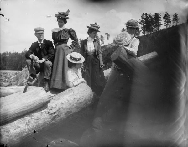 A group of five women and one man pose among logs on a shoreline.
