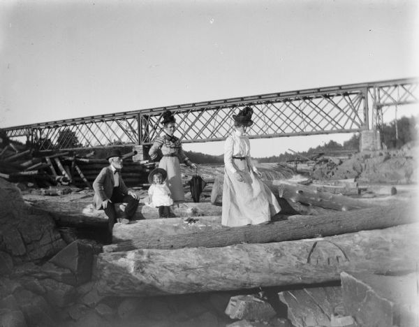 A man, two women, and a young child sit or stand among a large number of logs.