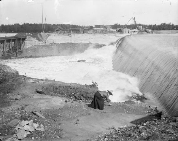 A woman gathers stones at the bottom of a falls near a dam, probably the Hatfield Dam.
