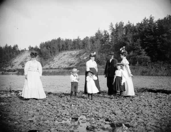 A family with young children stands on the rocky shoreline of a river.
