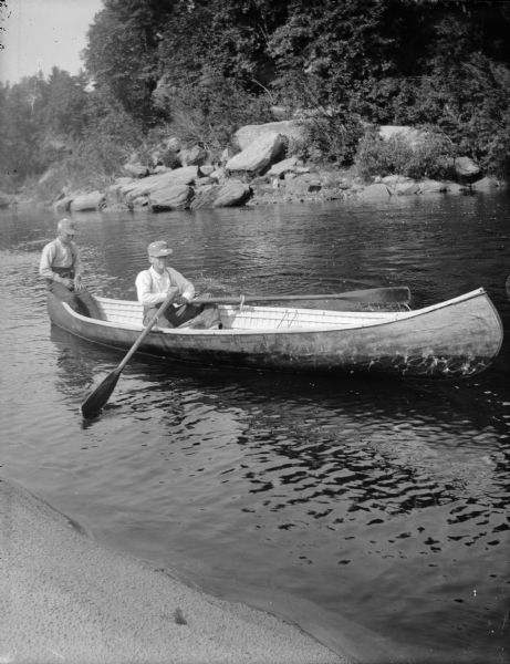 Two boys sit in a canoe. One boy rows with oars and the other sits in the bow.