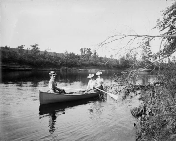 Three women sit in a rowboat on a river.