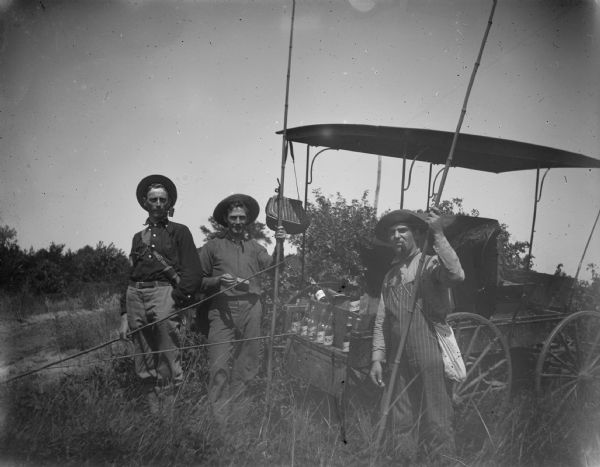 Three fisherman pose next to a wagon carrying glass bottles. The man on the far right is probably August Anderson.