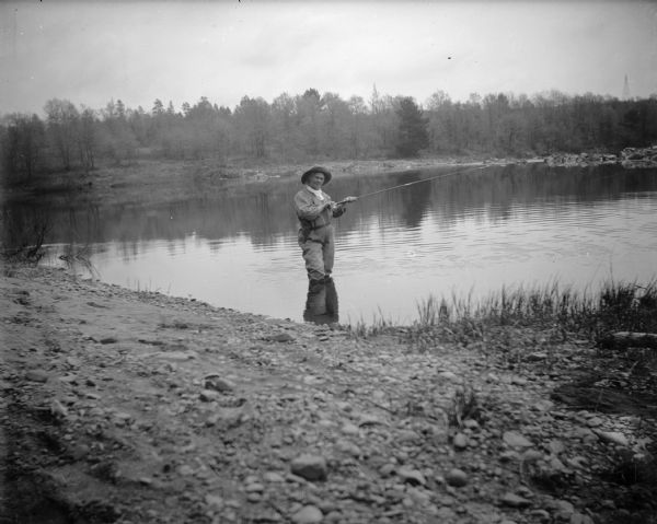 A fisherwoman? stands knee deep in a river, presumably trout fishing.