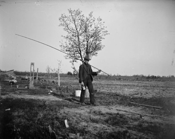 A young man walks with a large fishing pole and a can, presumably a can of worms.