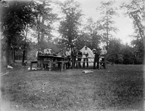 A group of men pose with pots and pans outside of a tent, probably at the present day site of Perry Creek Park.