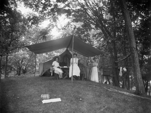 Three women and a man rest under a tent awning.