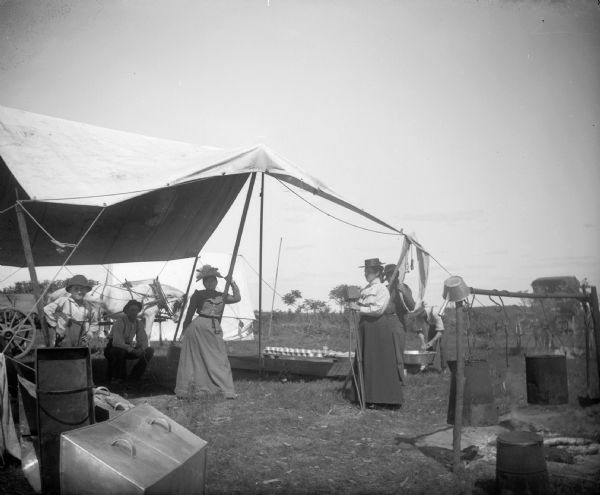 A group of men, women, and children gather outside a tent. One of the women attends to a camera.