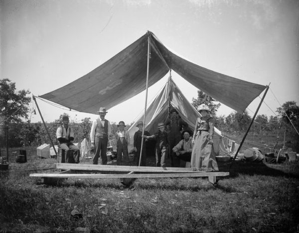 A group of men, women, and children pose under a tent awning.
