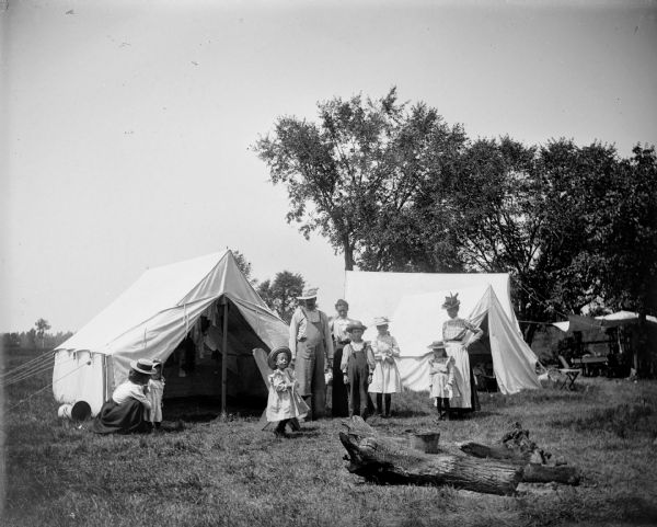 Three women, a man and several children pose outside of two large tents.