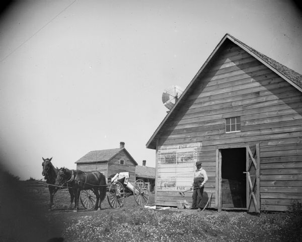 A man papers a barn with posters for the "Black River Falls Fair, September 7, 8, 9 & 10."