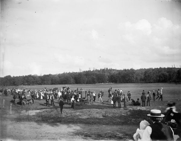 A large group of men, women, and children gather in a field.