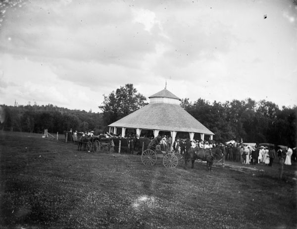 A large crowd gathers under a pavilion in a field.
