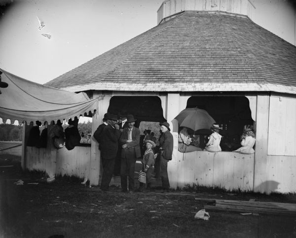 A group of men, women, and children mingle in an outdoor pavilion.