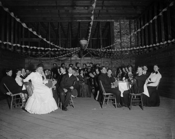 A large group of men and women sit for a banquet in an unfinished building.