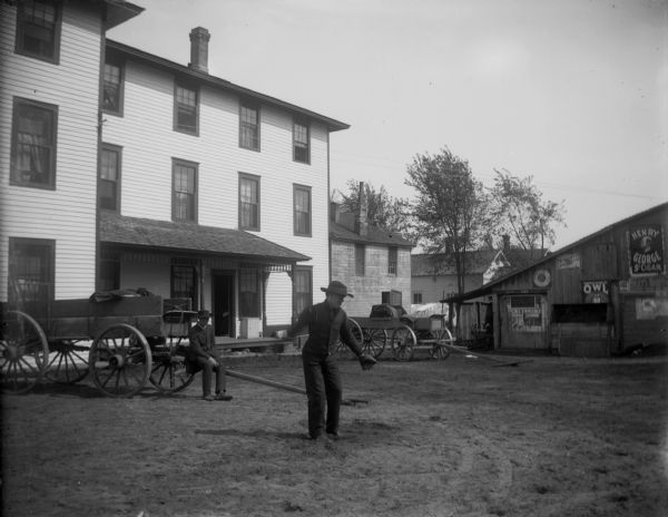 A man throws a baseball on a street in town, probably in front of the Merchants Hotel barn.