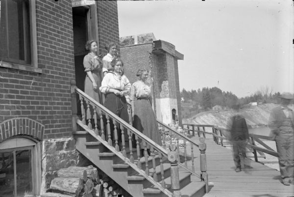 Four telephone operators pose on the steps of the Black River Falls Exchange Office Building. The second woman from the bottom is probably Mrs. W.E. (Hagen) Parsons. Possibly taken just after the flood of 1911, for the building next door is damaged.