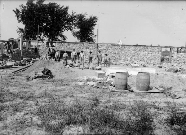 Two horses, several men and two youth stand in front of a stone wall or foundation. The men could be reconstructing a barn after the flood of 1911.