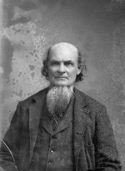 A studio portrait of an elderly man with a long beard wearing a suit jacket and vest.