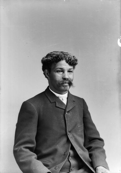 A studio portrait of an unidentified African-American man with curly hair and a moustache. He is wearing a suit jacket and vest.