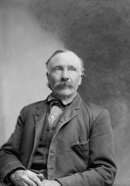 A studio portrait of an elderly man with a moustache wearing a suit jacket, vest, and necktie.
