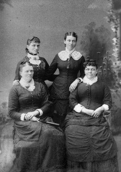 A studio portrait of four women in front of a painted backdrop. Two women sit while two others stand behind them.
