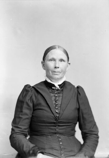 A seated woman wearing a black dress poses for a studio portrait.