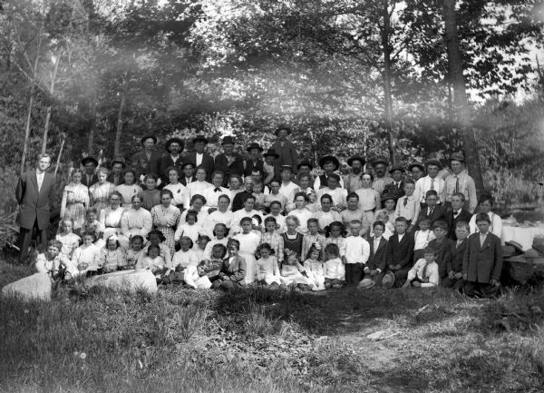 An outdoor portrait of a large group of men, women, and children on a trail or path among trees. Possibly a family reunion or other gathering.