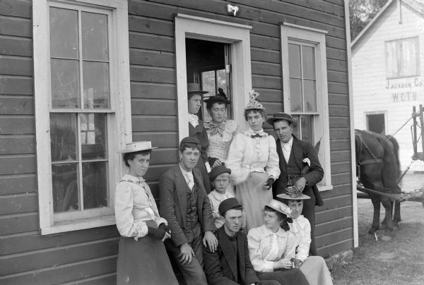 A group of three men, six women, and a child gathered in the doorway of a building. Another building in the background has "Jackson Co. W.C.T.U." written on it (perhaps the Women's Christian Temperance Union), and "Dining Hall" written above the doorway.