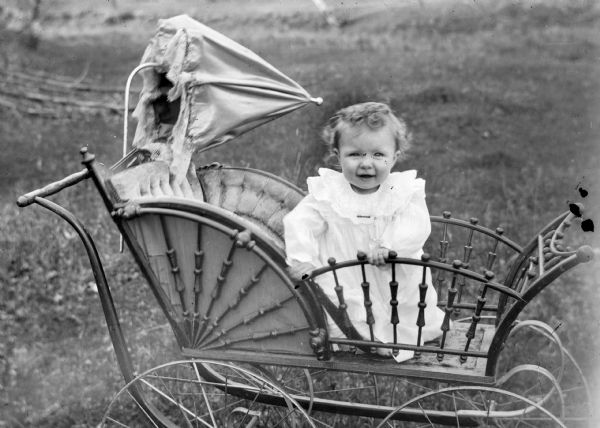 An outdoor portrait of an infant seated in a baby carriage with an umbrella attached to the back.