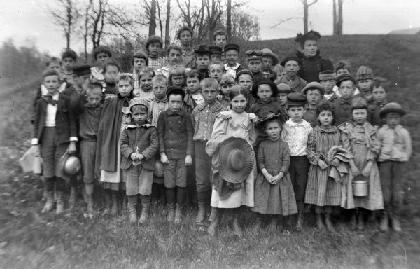 Group portrait of a large group of children with a woman standing outside on a hill.