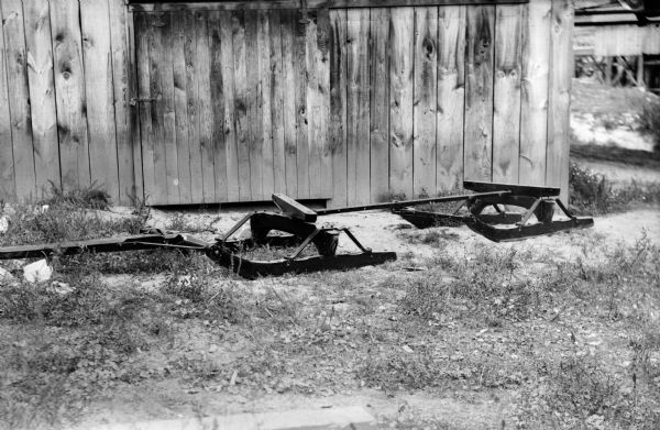 An empty bobsled, possibly a Spaulding Oscillating bobsled manufactured by P.R. Olson, in front of a wooden building.