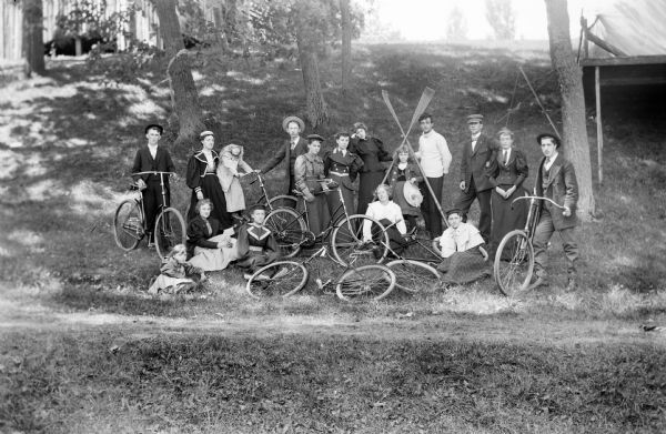 A group of seventeen young people of varying ages posing outside against a hill with bicycles and a set of rowing oars.