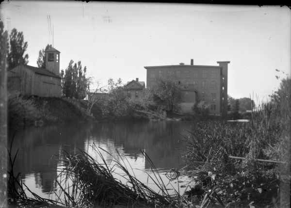 Brick and wooden buildings by a marshy riverbank.