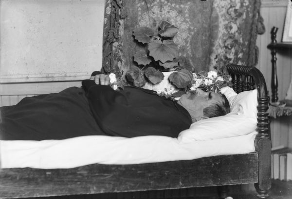 Portrait of a deceased man lying in state on a bed.