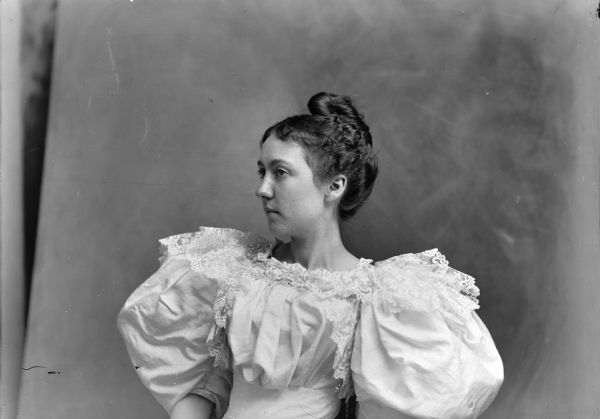 Studio portrait of a seated young woman wearing a dress with a lace collar and large, puffy sleeves.