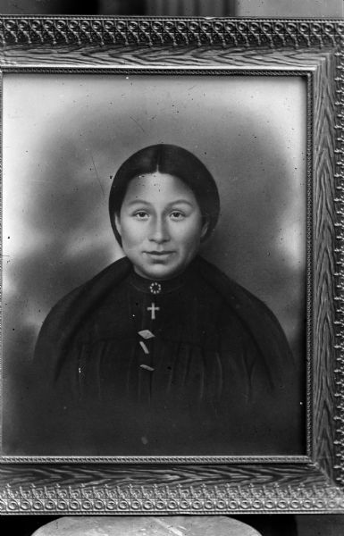 Copy photograph of a framed painted portrait of a Ho-Chunk woman wearing a blouse, shawl, and many brooches. Possibly a member of the peyote religion.