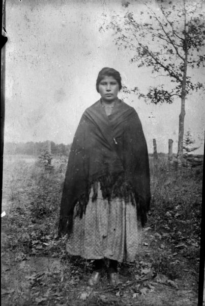 Copy photograph of a Ho-Chunk woman posing standing in a field, wrapped in a fringed shawl.