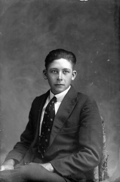 Studio portrait of a young Ho-Chunk man with short hair posed sitting and wearing a suit and necktie.